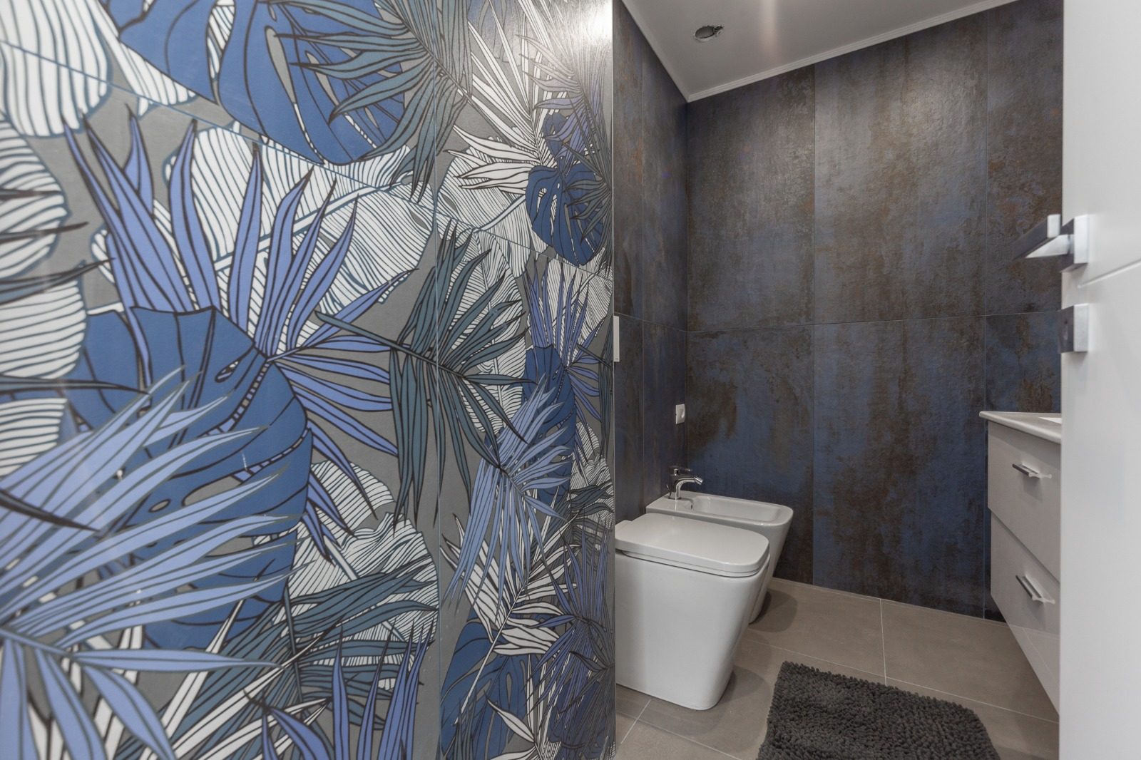 Bagno con parete decorata a foglie e sanitari sospesi