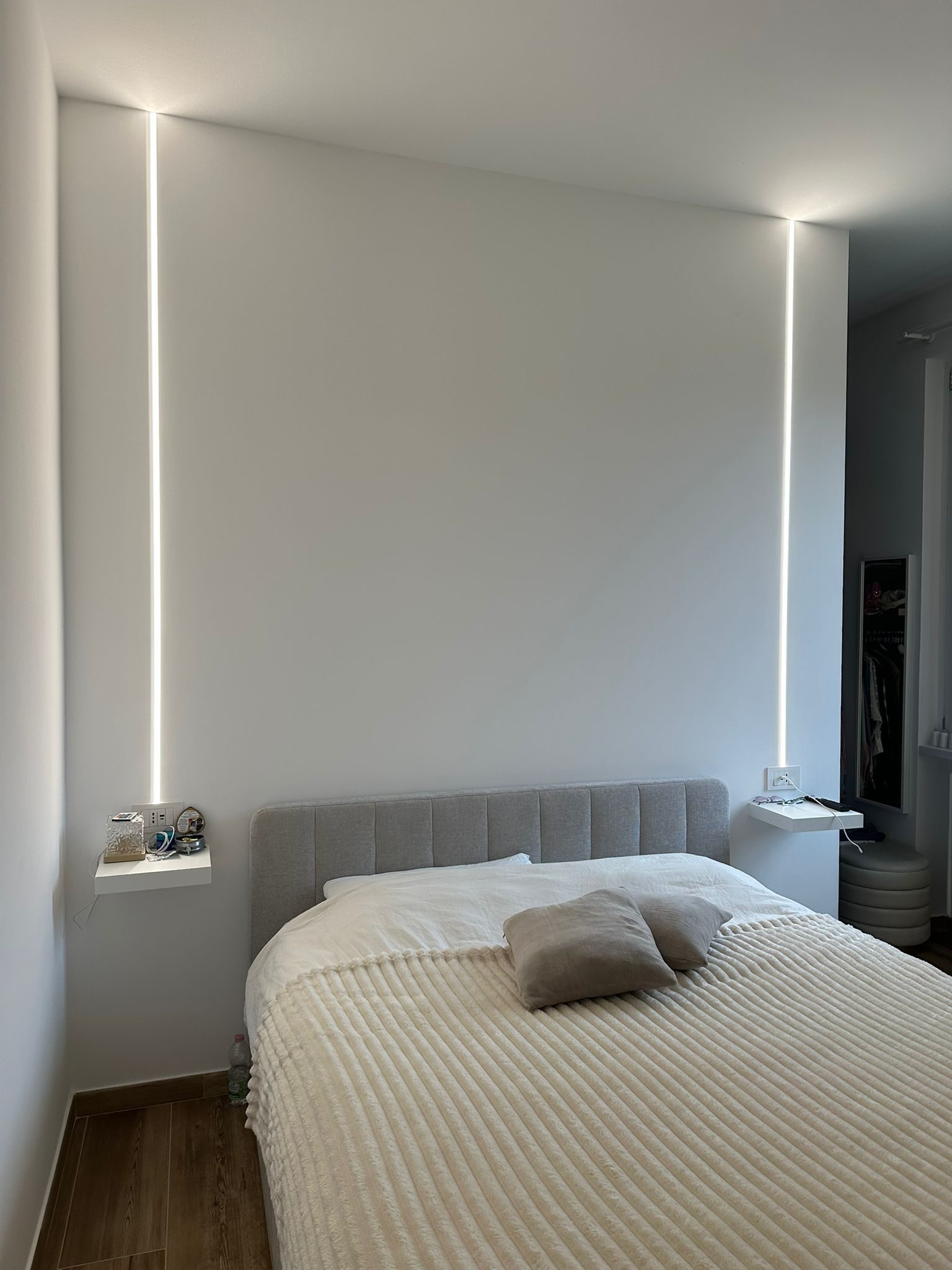 Camera da letto con strisce LED verticali a incasso, comodini sospesi e pavimento effetto legno