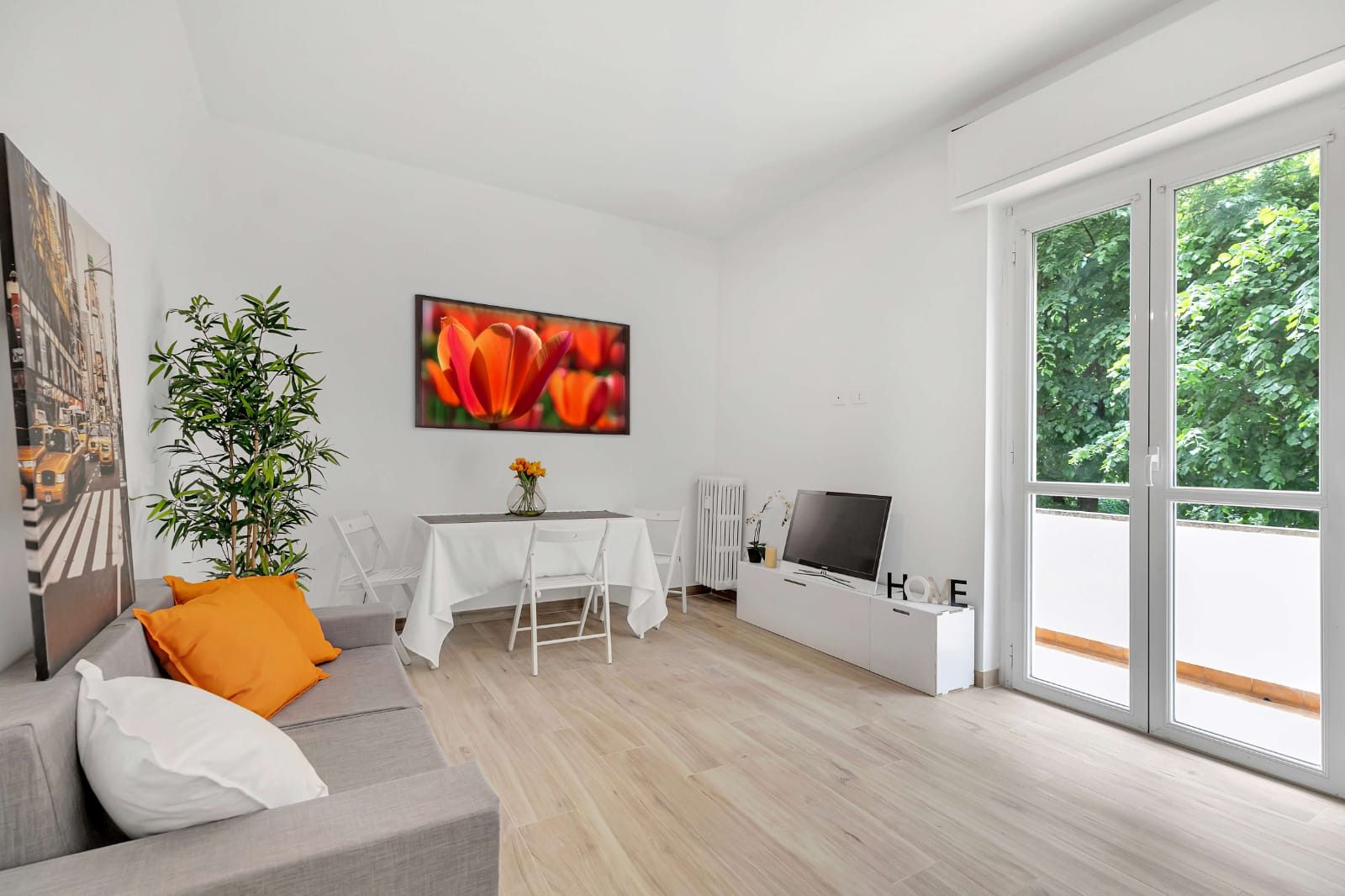 Soggiorno bianco con divano grigio, tavolo apparecchiato, mobile TV e portafinestra aperta sul balcone