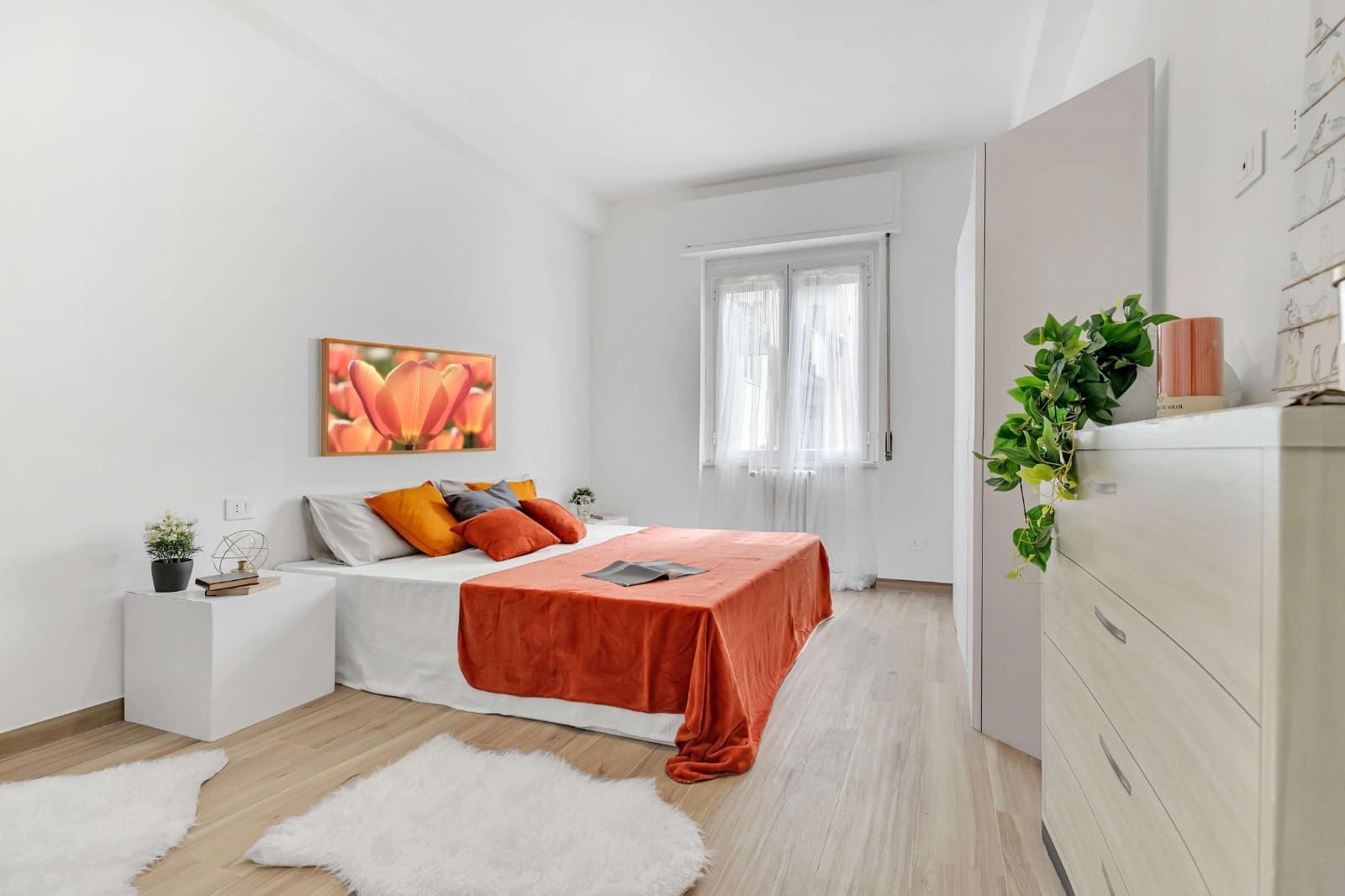 Camera matrimoniale con letto, copriletto arancione, armadio, cassettiera e finestra con tenda bianca