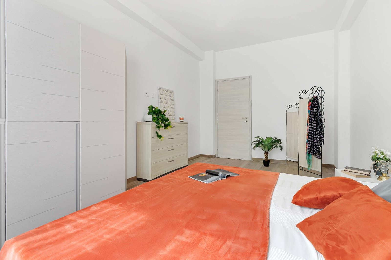 Camera da letto con armadio bianco, cassettiera in legno chiaro, porta interna e pavimento effetto legno