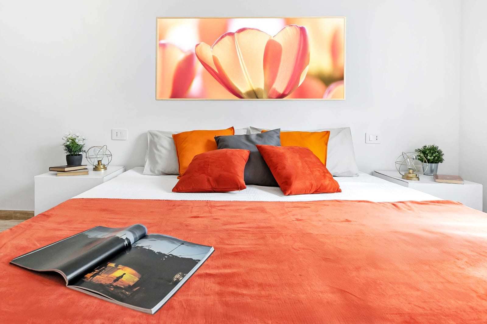 Letto matrimoniale visto di fronte, quadro sopra la testiera, comodini bianchi e prese a parete