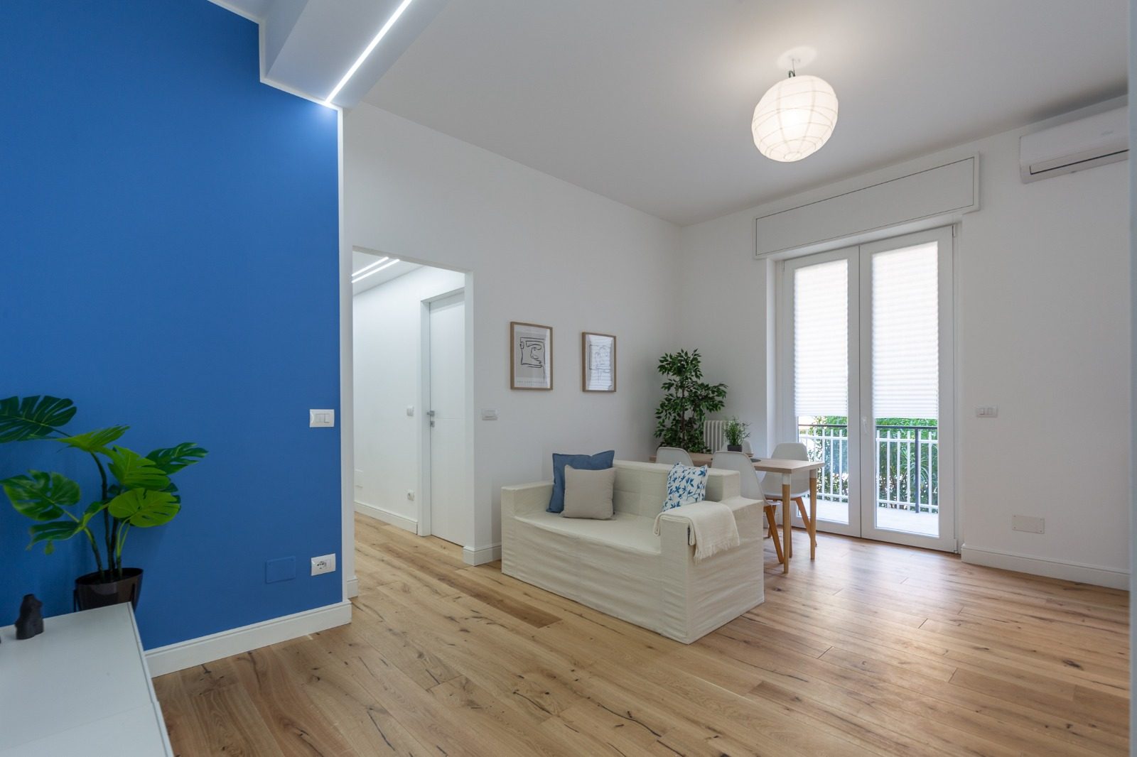 Soggiorno con parete blu, parquet in rovere, luce lineare a soffitto e portafinestra sul balcone