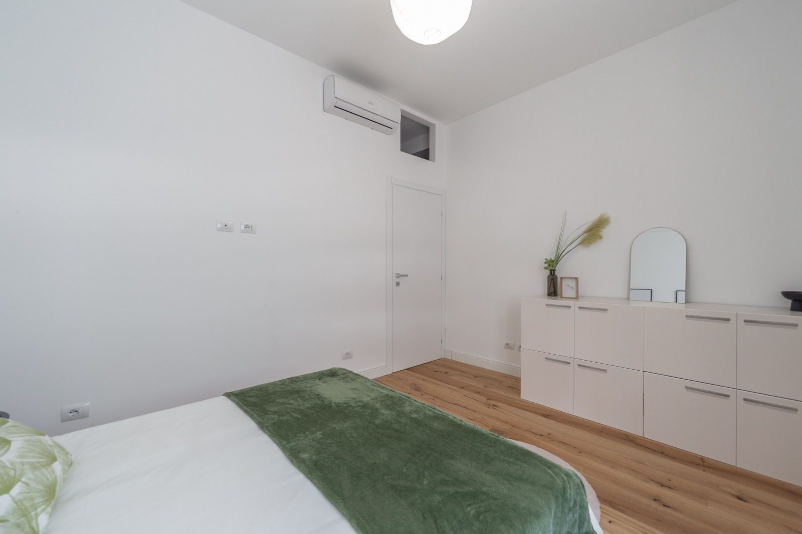 Camera da letto con unità interna del climatizzatore a parete, porta bianca e mobili contenitori