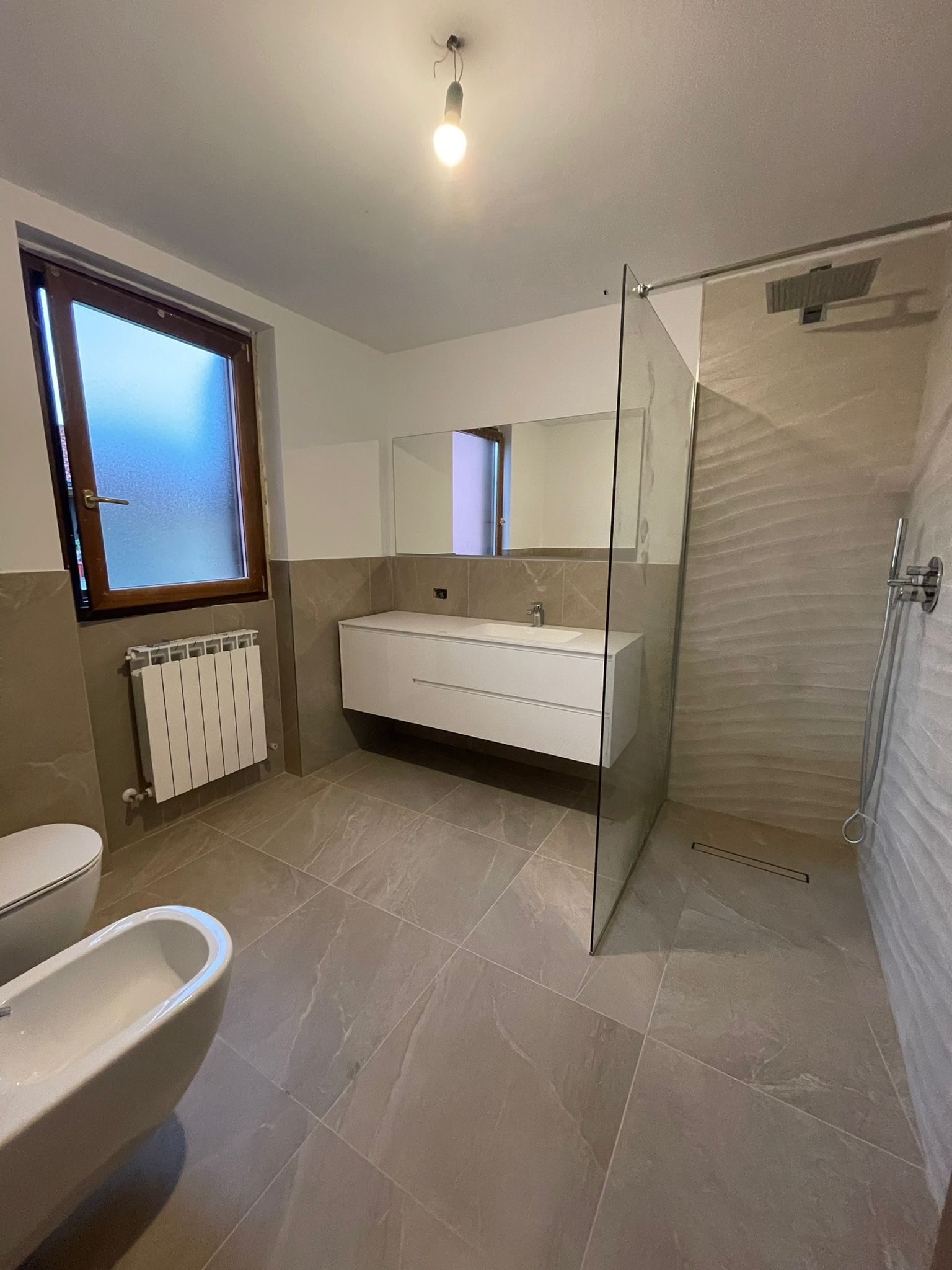 Bagno con vasca, mobile lavabo sospeso e parete in gres effetto pietra
