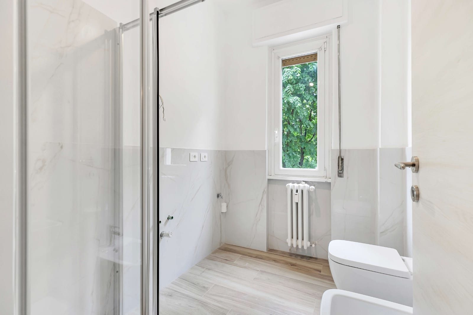 Bagno con box doccia in cristallo, rivestimento effetto marmo, wc e bidet sospesi, finestra