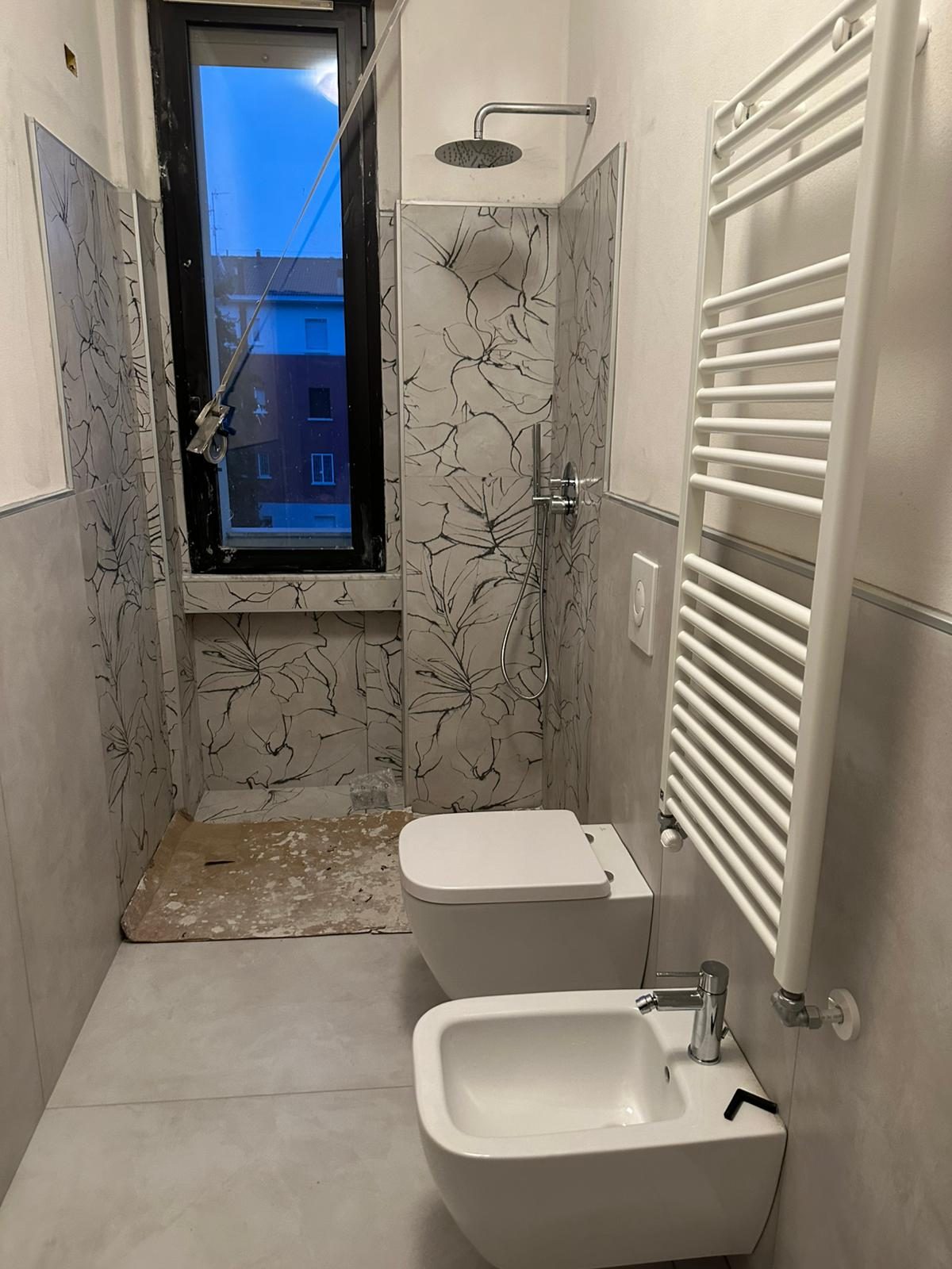 Bagno in ultimazione con sanitari sospesi, scaldasalviette a parete e nicchia doccia con rivestimento decorato.
