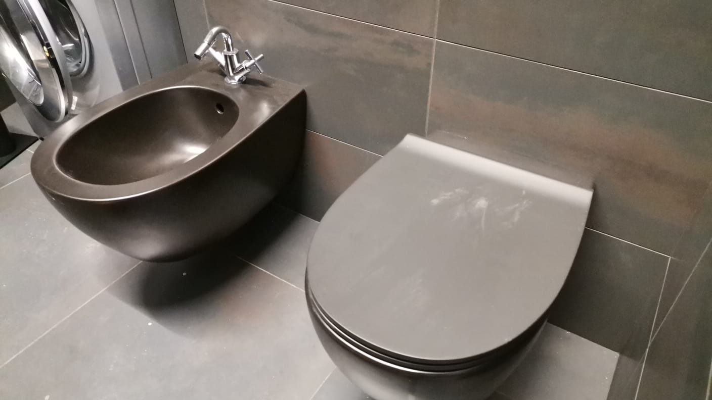 Bidet e vaso sospesi scuri in un bagno con gres grigio e lavatrice