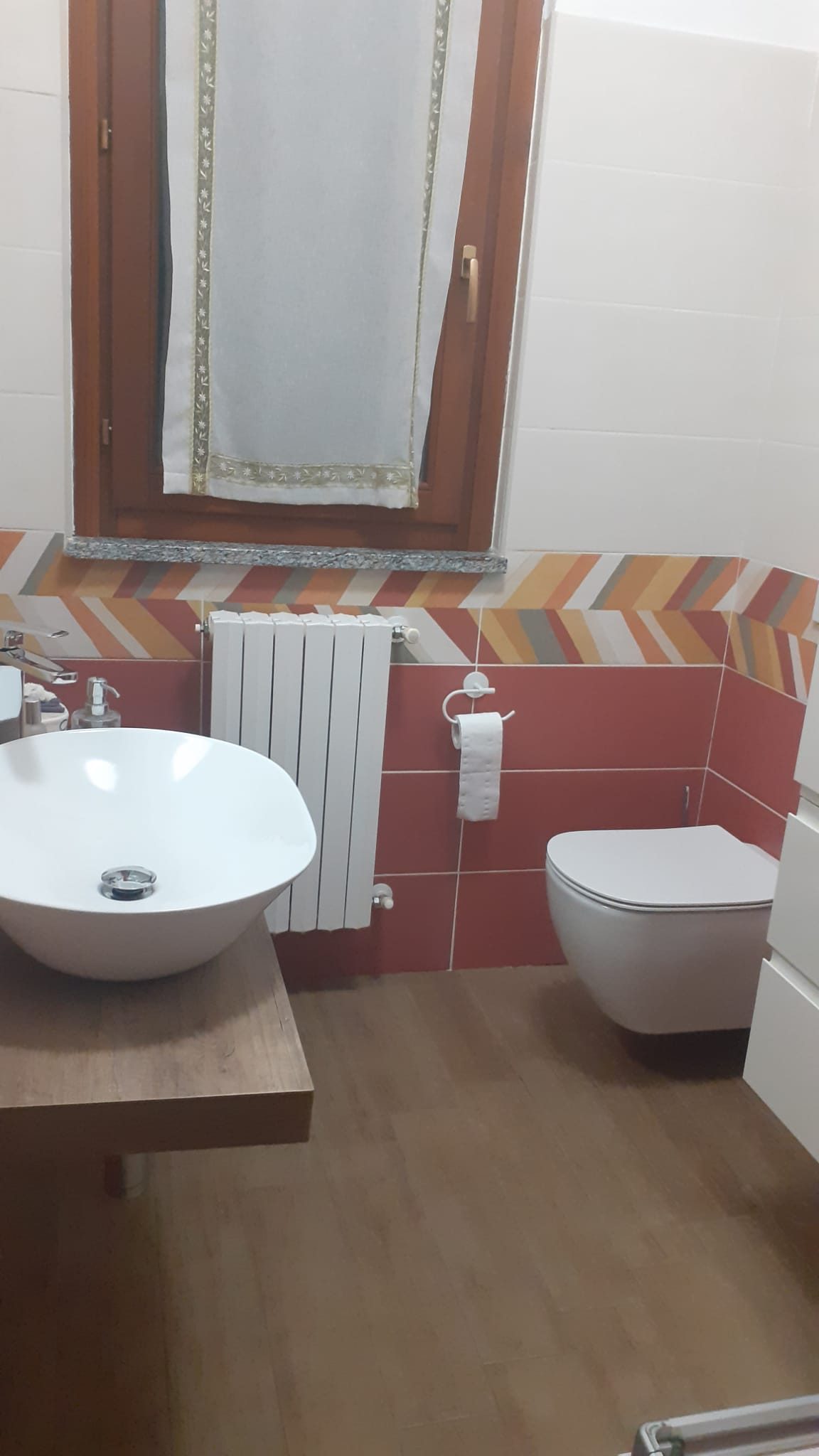Bagno finito con lavabo bianco d'appoggio su mensola in legno, vaso sospeso e radiatore