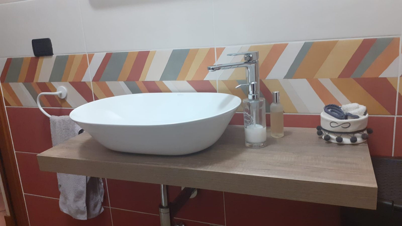 Lavabo ovale bianco da appoggio su mensola in legno, miscelatore cromato e piastrelle decorate a chevron
