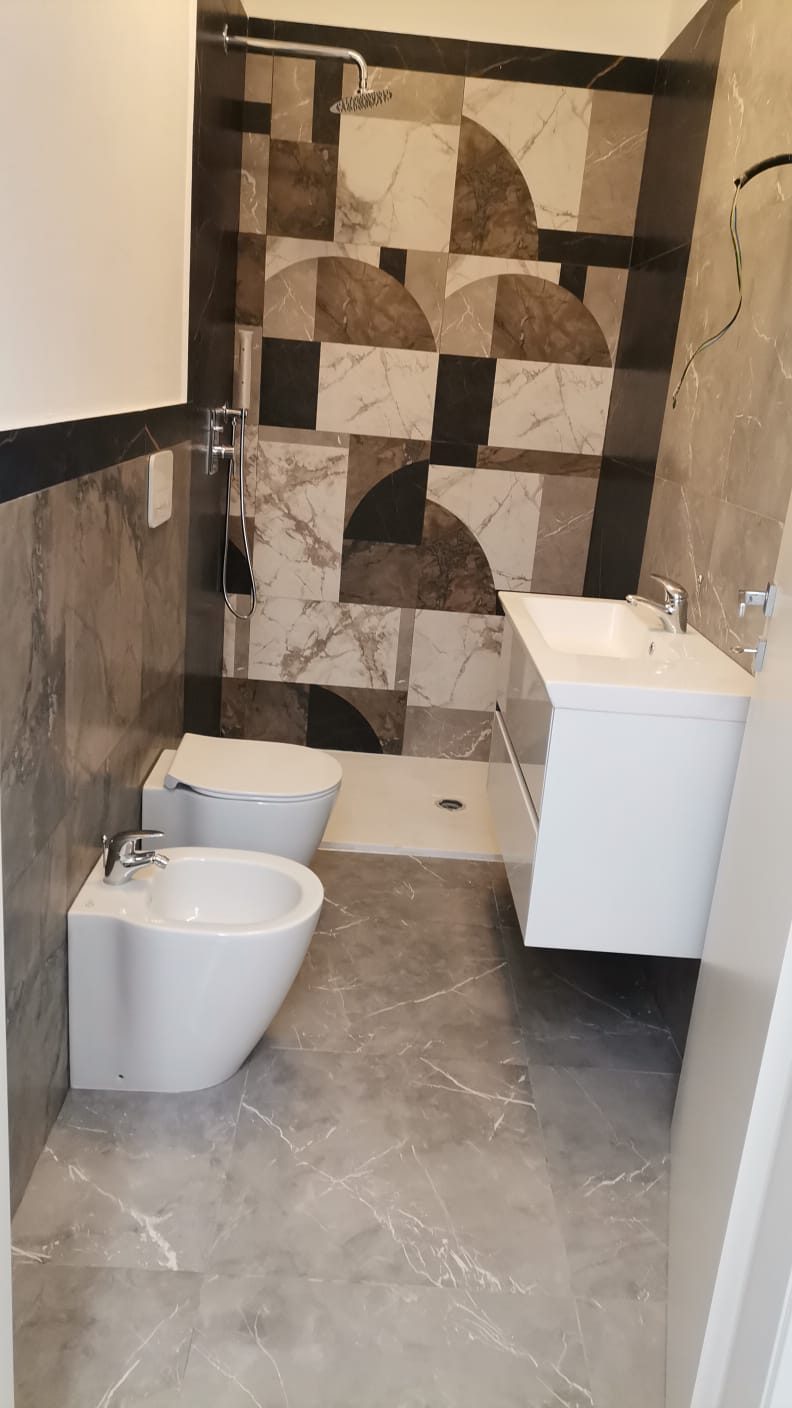 Bagno finito con rivestimento in gres effetto marmo, piatto doccia, mobile lavabo sospeso, wc e bidet