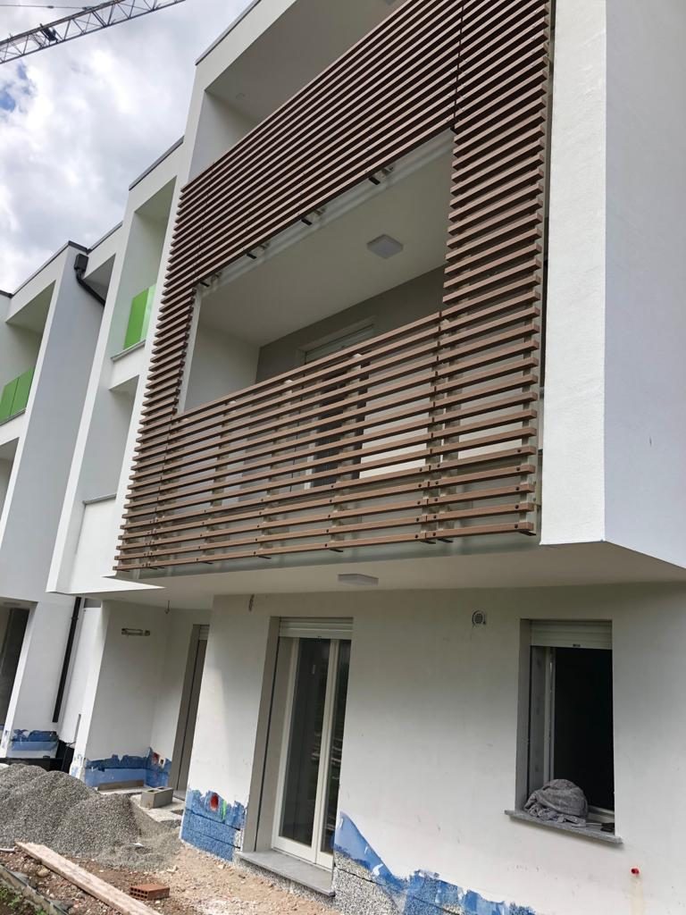 Facciata di villette a schiera in costruzione con frangisole in listelli di legno sul balcone