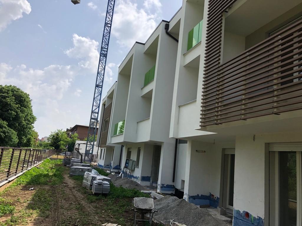 Fila di case a schiera in costruzione vista dal giardino, gru e materiali a terra