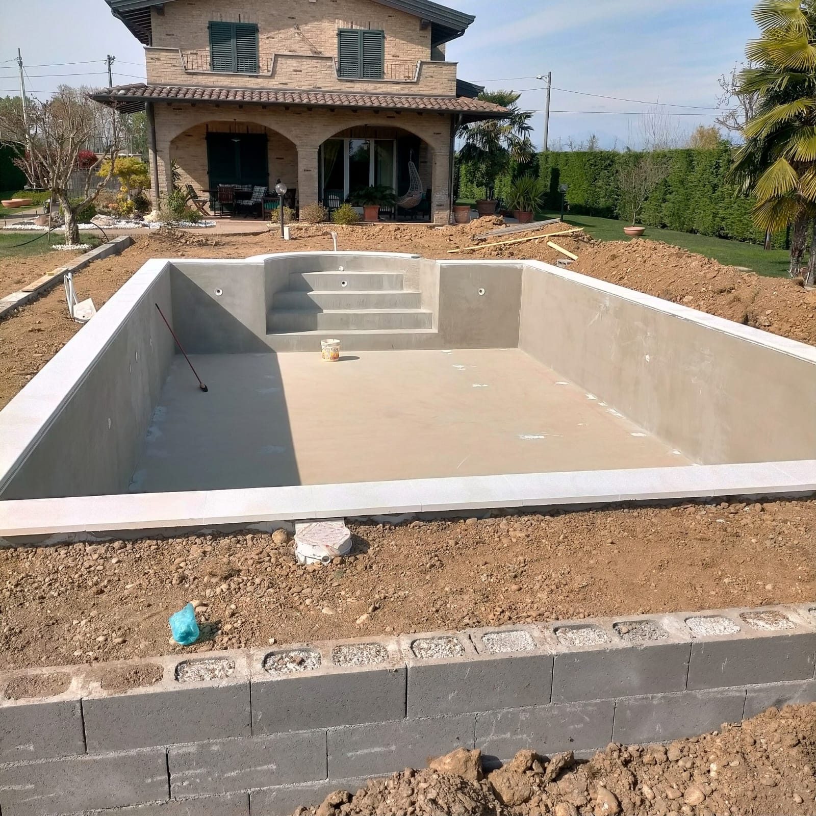 Piscina interrata rasata con bordo posato e muro in blocchi di cemento in primo piano