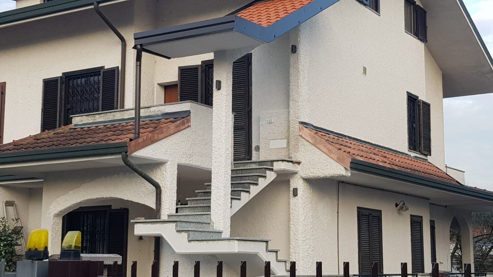 Edificio residenziale intonacato di bianco con scala esterna, persiane scure e tetto in coppi
