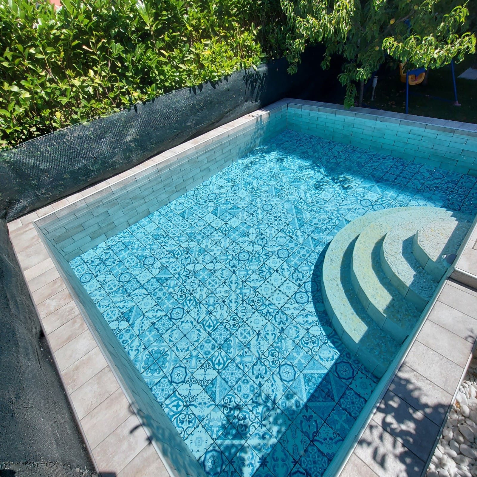 Vasca della piscina vista dall'alto: fondo con piastrelle decorate blu e gradini curvi d'ingresso