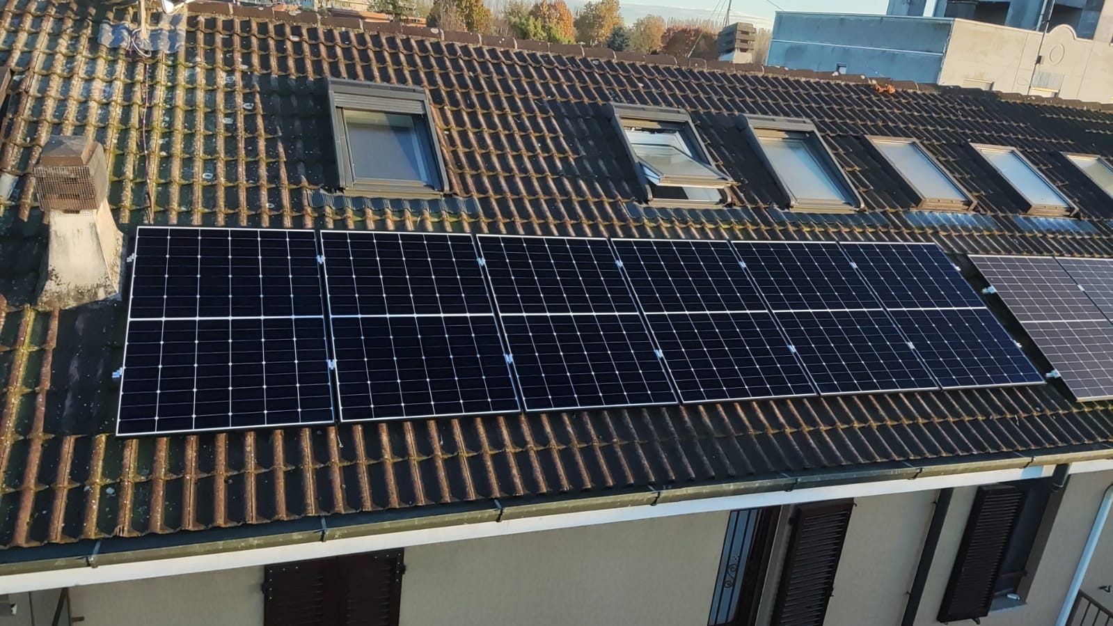 Vista dall'alto del tetto: fila di moduli fotovoltaici, camino in muratura e finestre da tetto