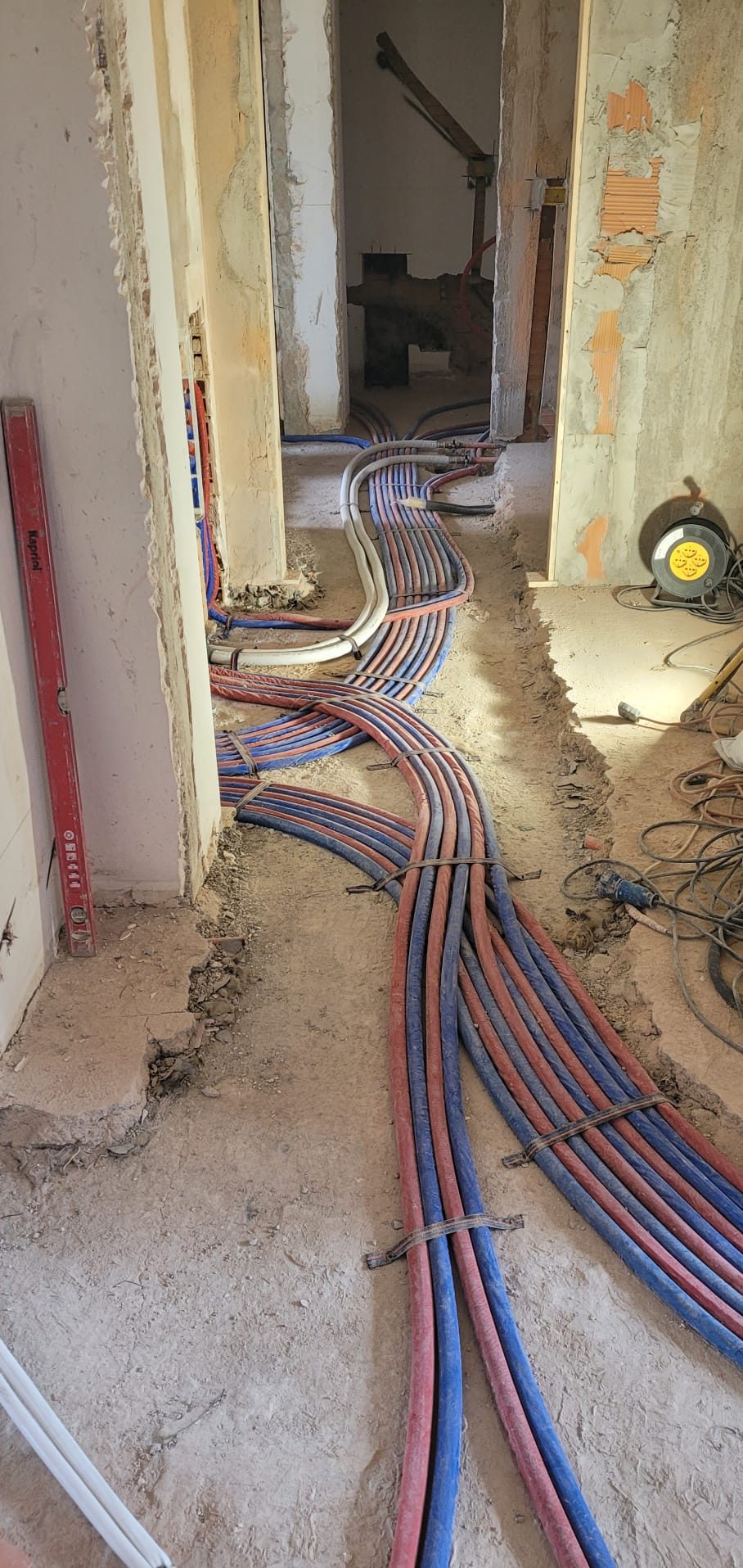 Corridoio in ristrutturazione con fasci di tubi rossi e blu posati a pavimento verso le stanze.