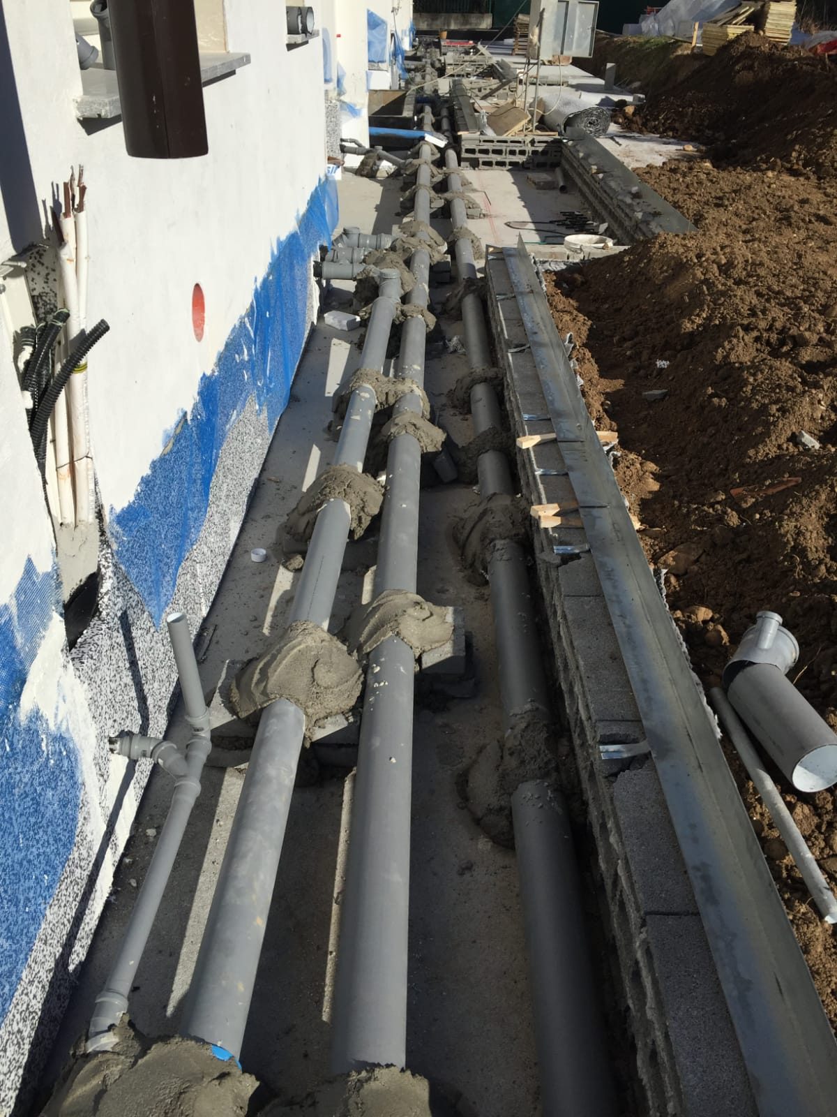 Tubazioni grigie di scarico posate lungo il perimetro esterno di un edificio in costruzione
