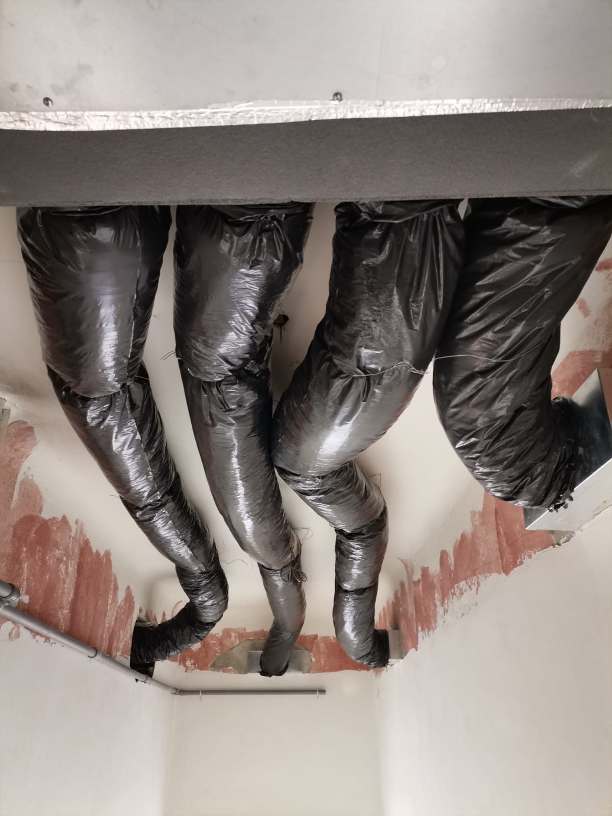 Quattro canali flessibili coibentati neri sotto il soffitto, collegati a plenum in lamiera