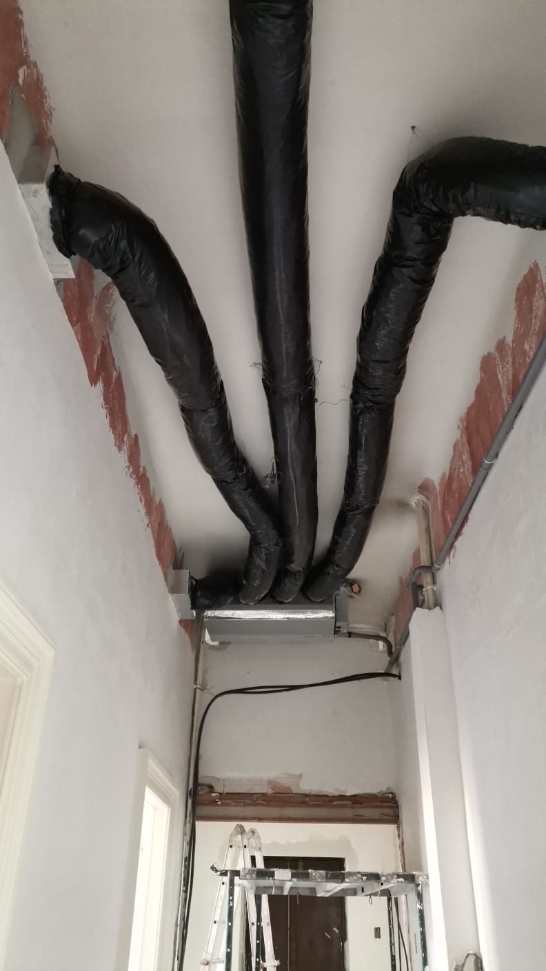 Corridoio in cantiere, tre canali flessibili neri convergono in un plenum in lamiera a soffitto