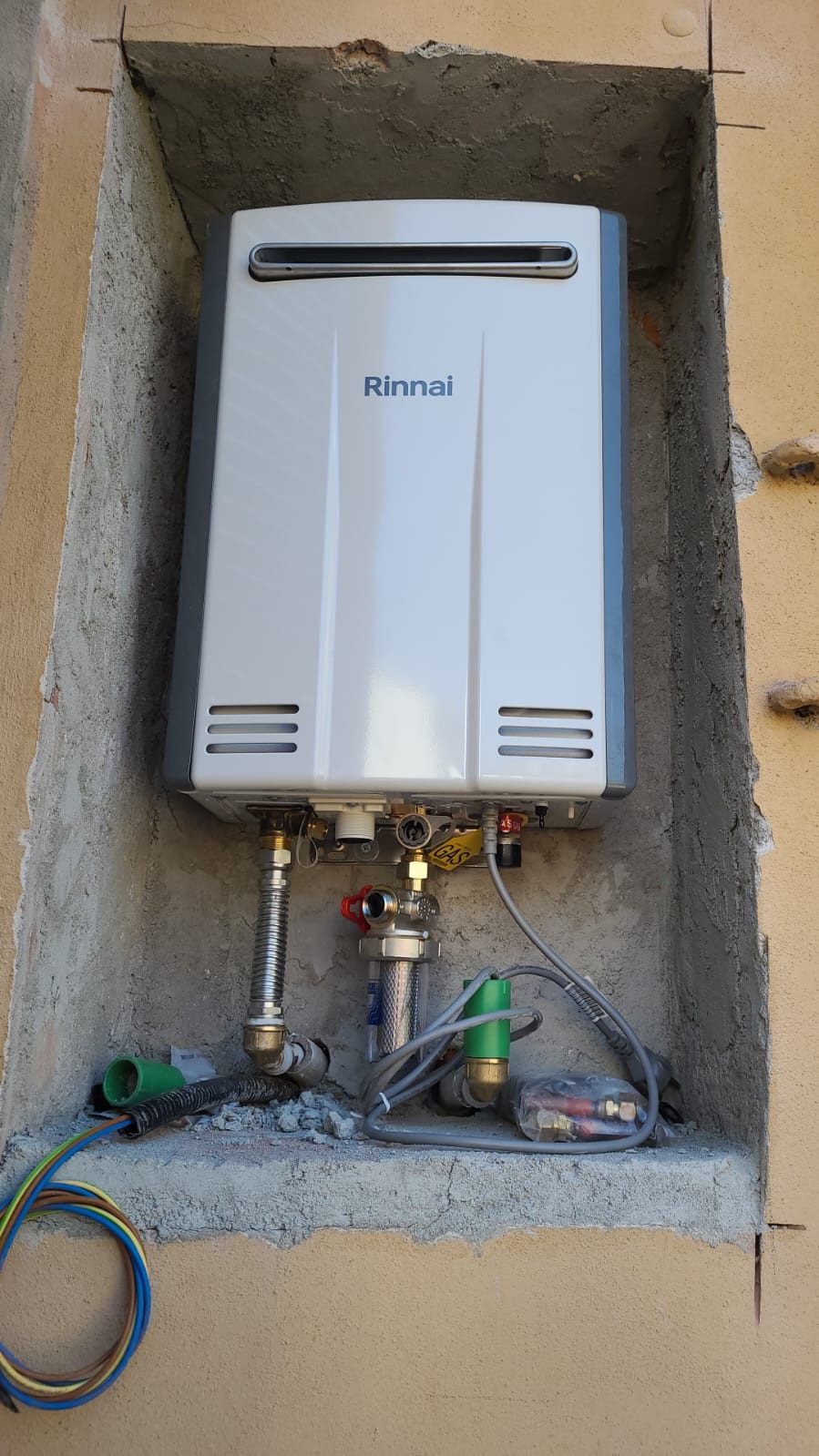 Scaldabagno a gas installato in una nicchia della facciata, con allacci idraulici e cavi ancora scoperti
