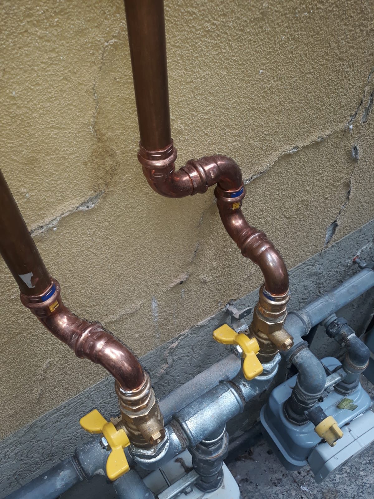 Tubazioni in rame con raccordi a pressare collegate a due contatori del gas con valvole gialle