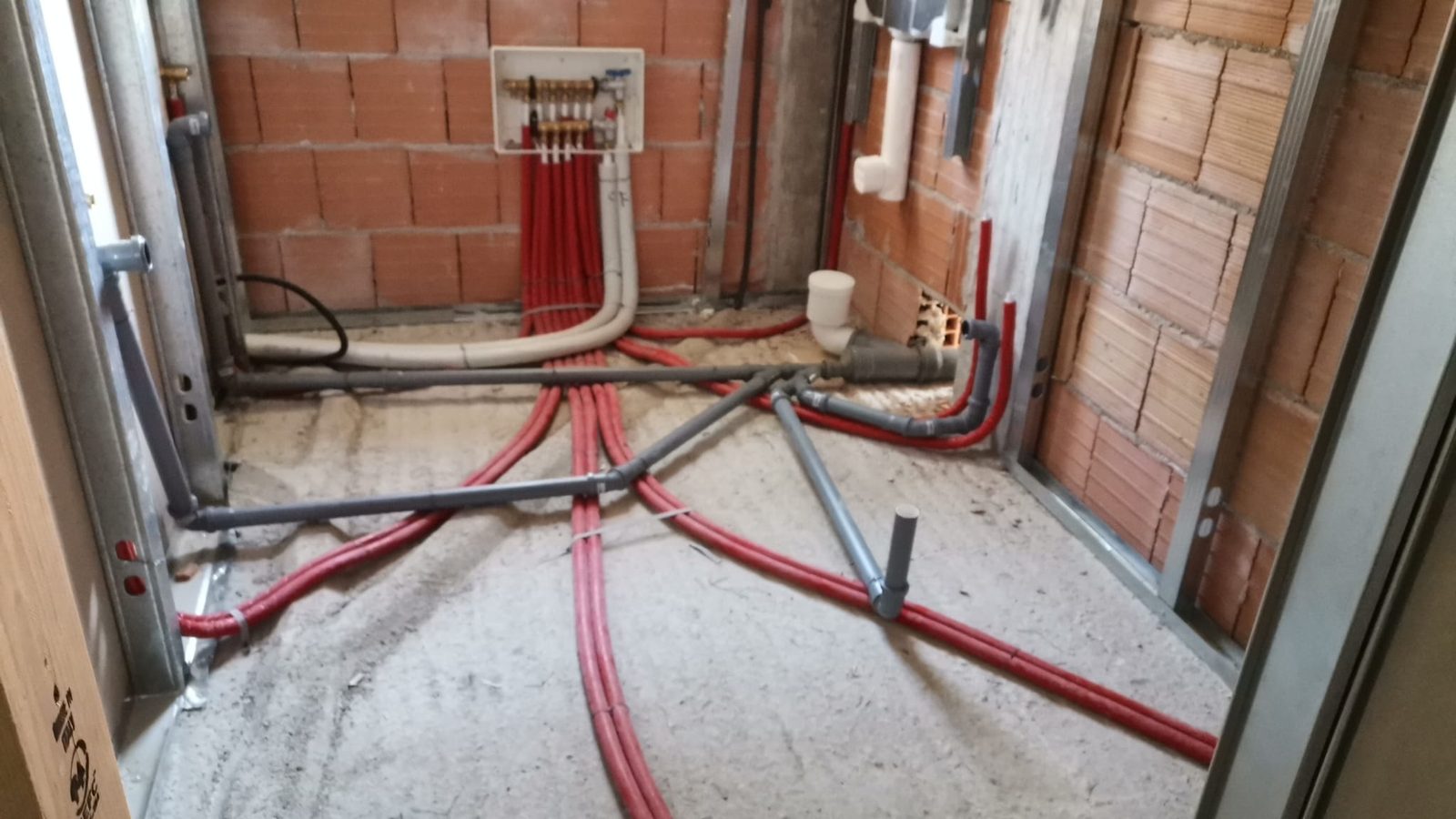 Cantiere: collettore idrico in nicchia, tubi in guaina rossa e scarichi in PVC sul solaio