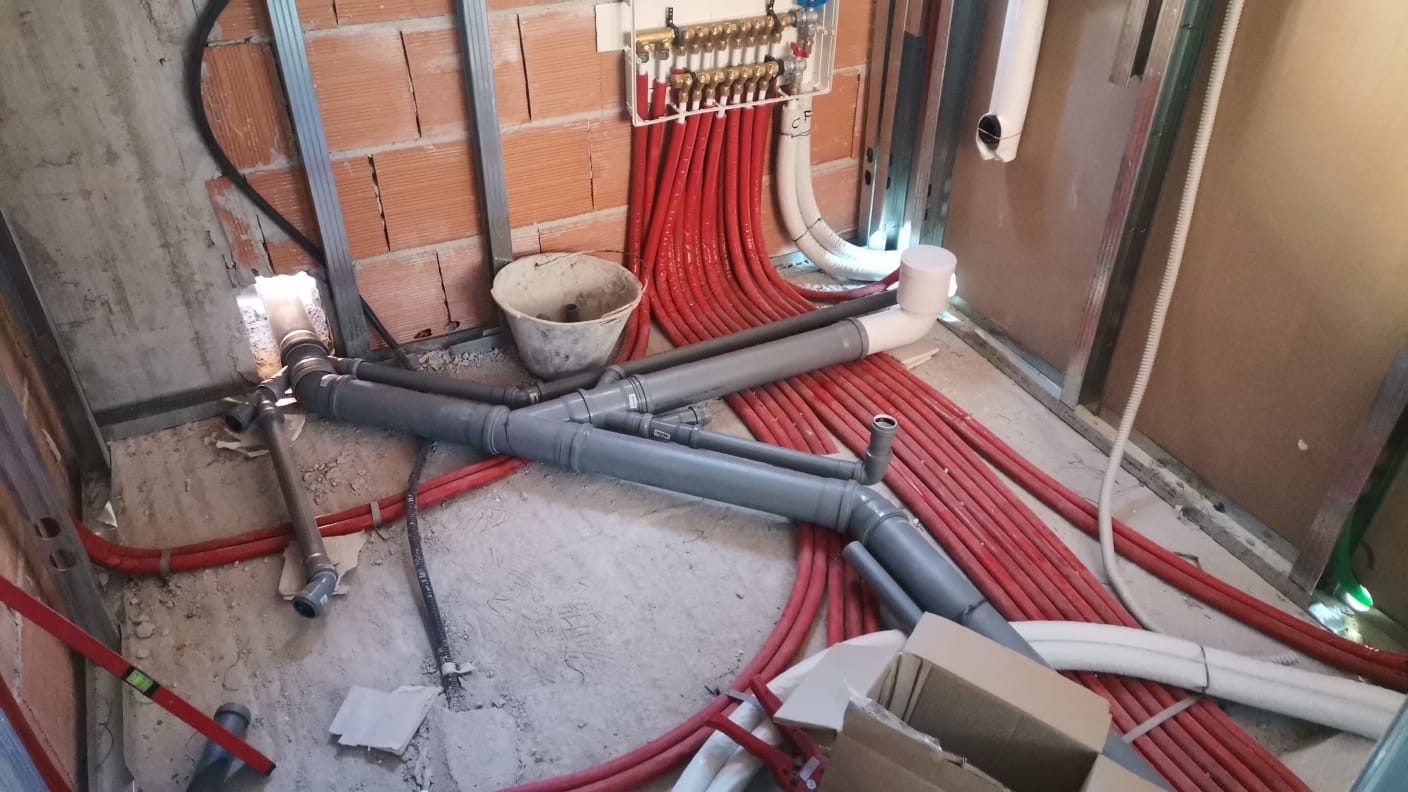Posa impianti: fascio di tubi in guaina rossa e tubazioni di scarico in PVC a pavimento