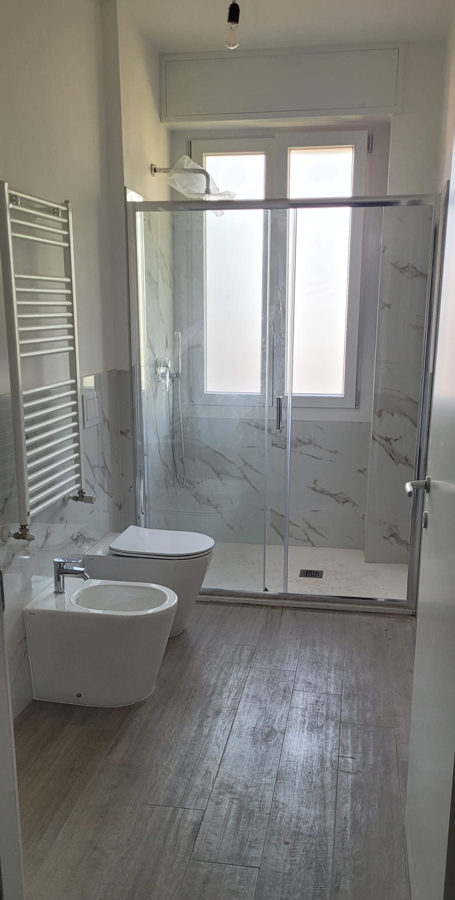 Bagno completo con sanitari sospesi, scaldasalviette e pavimento effetto legno